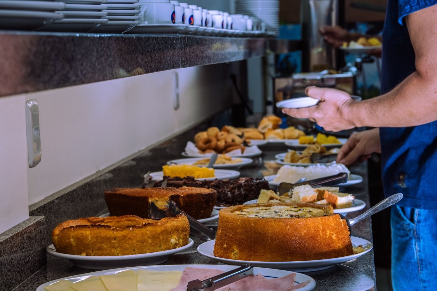 Hóspede sendo servido no buffet de bolos do café da manhã